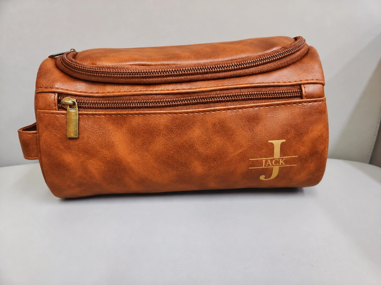 Cognac toiletry bag with gold J and JACK monogram on a table