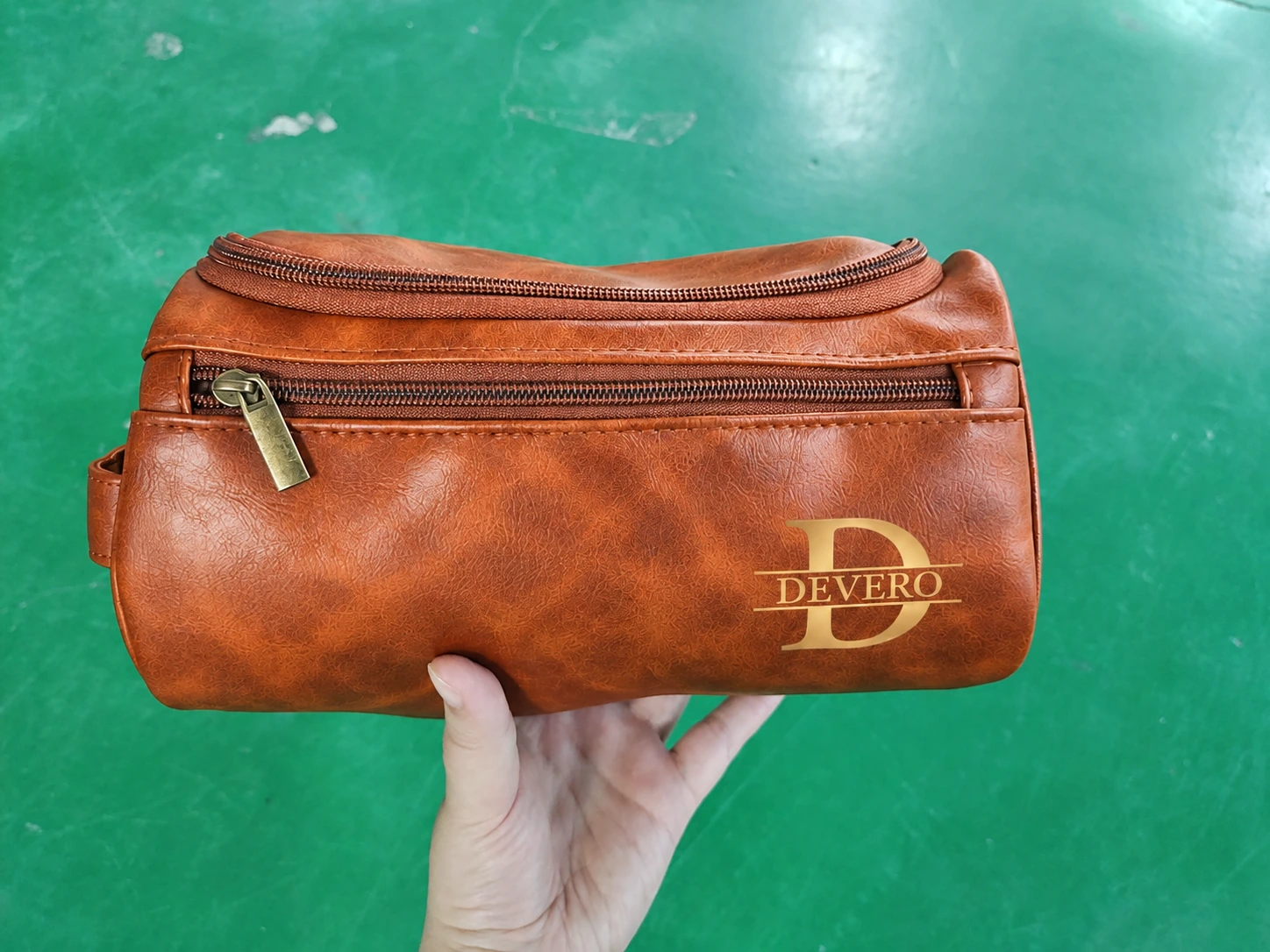 Cognac toiletry bag with gold D and DEVERO monogram held in one hand